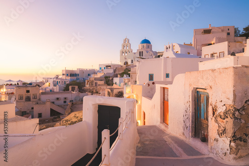 A narrow old town lane in the quaint village of Pyrgos Kallistis leads to the traditional blue dome Greek Orthodox Saint George Church on the island of Santorini, Greece at sunset.