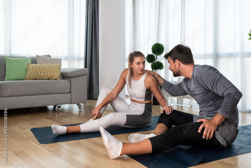 Obraz premium Young active couple exercising in their home with yoga mats stretching their muscles. Wife and husband workout training to reduce stress after day at work.