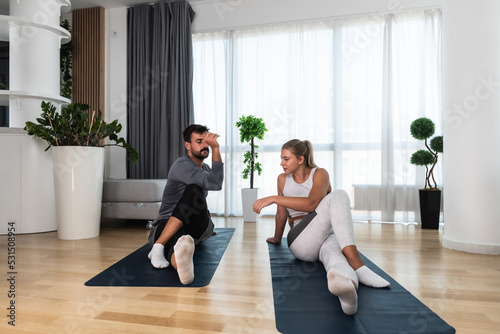 Young active couple exercising in their home with yoga mats stretching their muscles. Wife and husband workout training to reduce stress after day at work.