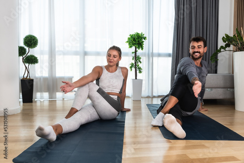 Fototapeta Naklejka Na Ścianę i Meble -  Young active couple exercising in their home with yoga mats stretching their muscles. Wife and husband workout training to reduce stress after day at work.