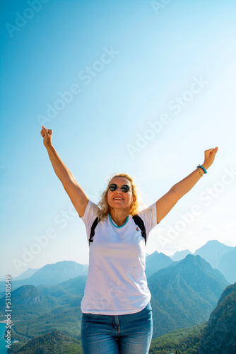Happy celebrating winning success woman at sunset or sunrise standing elated with arms raised up above her head in celebration of having reached mountain top summit goal during hiking travel trek.