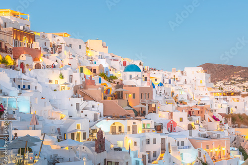 Seaside view at blue hour of traditional white wash buildings and blue dome churches at the popular seaside tourist resort village of Oia on the Greek island of Santorini, Greece.