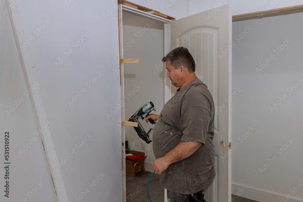 Installing interior doors in a new house is the job of a trim carpenter with worker using air nail gauge