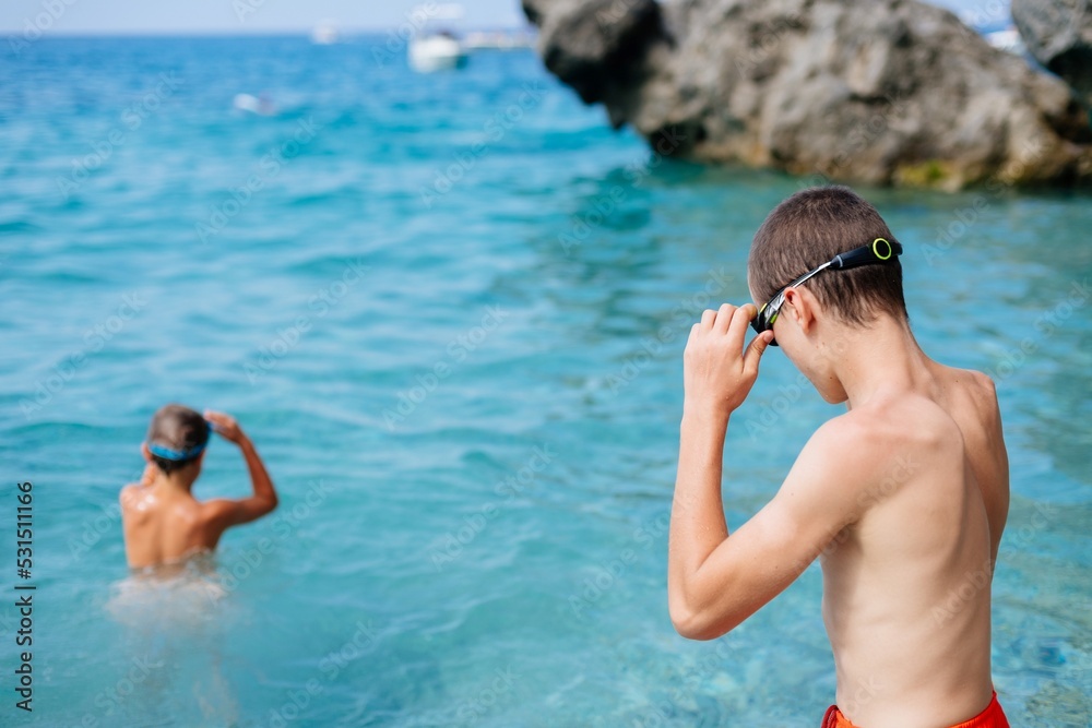 Teenage boy puts on his swimming googles and gets ready to swim in the sea, Corfu, Greece
