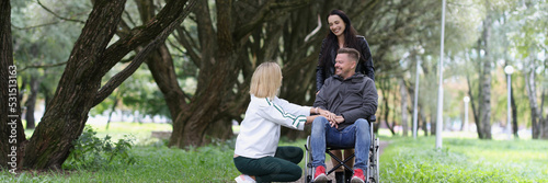Friends of woman and man in wheelchair communicate in park