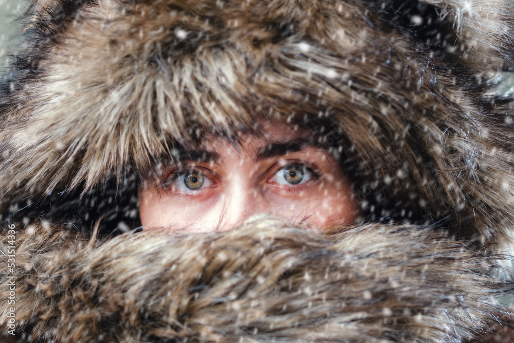Close-up of a woman in a fur hat made of natural or artificial fur. A wild female look through the wool. Snow and winter season Close-up of a woman in a fur hat made of natural or artificial fur. A wild female look through the wool. Snow and winter season