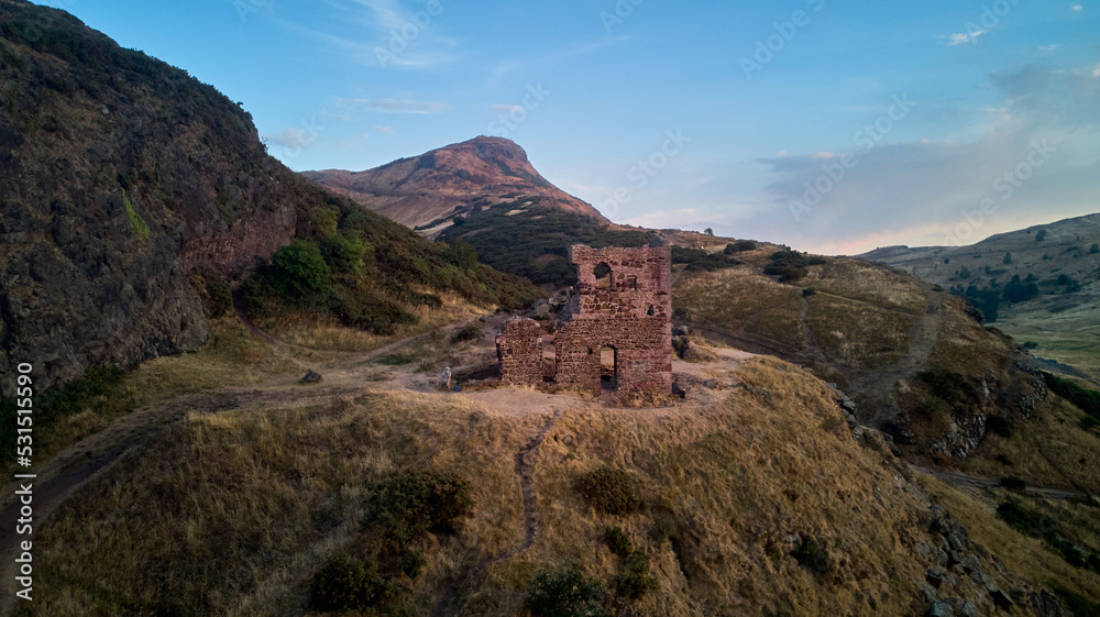 Ruin St Anthony Chapel with Arthur Seat at distance in summer evening- drone flight above Edinburgh