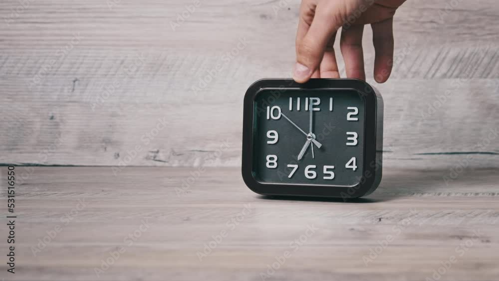 Pointer brown clock of square shape shows time on wooden table. Male