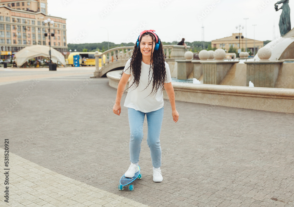 A beautiful young girl with dreadlocks rides a skateboard in sunny weather. generation z