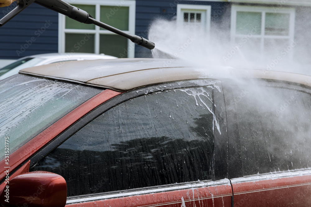 An man washing a car using high pressure water jets while cleaning the car is shown