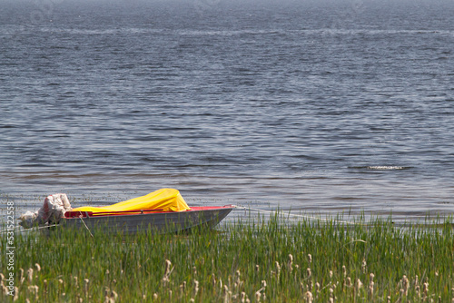 Boat moored on a river bank with green grass in the evening in spring in rural village area with trees reflecting in water