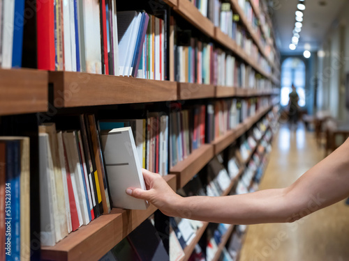 woman holding book in front of bookshelf, selective focus