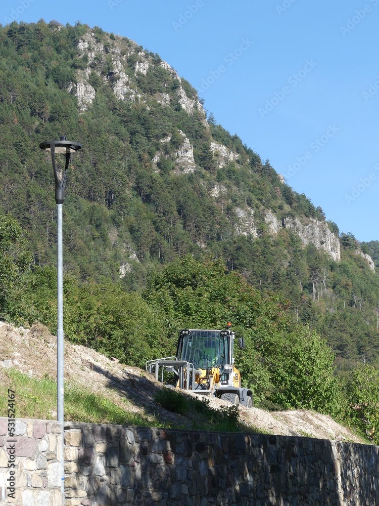 Fototapeta premium Bagger auf einer Baustelle hinter einer Steinmauer in den Alpen