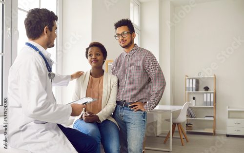 Young couple visiting doctor for professional consultation and health check up. Supportive gynecologist, OB GYN obstetrician or general practitioner talking to happy family about pregnancy planning