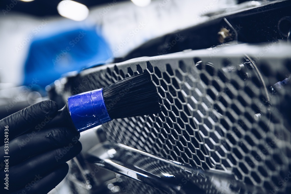 employee of a car detailing studio or a car wash cleans a car grill with a special brush. Car care