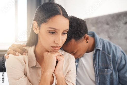 Upset couple fighting, arguing or breaking up while sitting on their bed in the bedroom at home. Sad man crying on the shoulder of his thinking wife while talking about divorce or difficult problems.