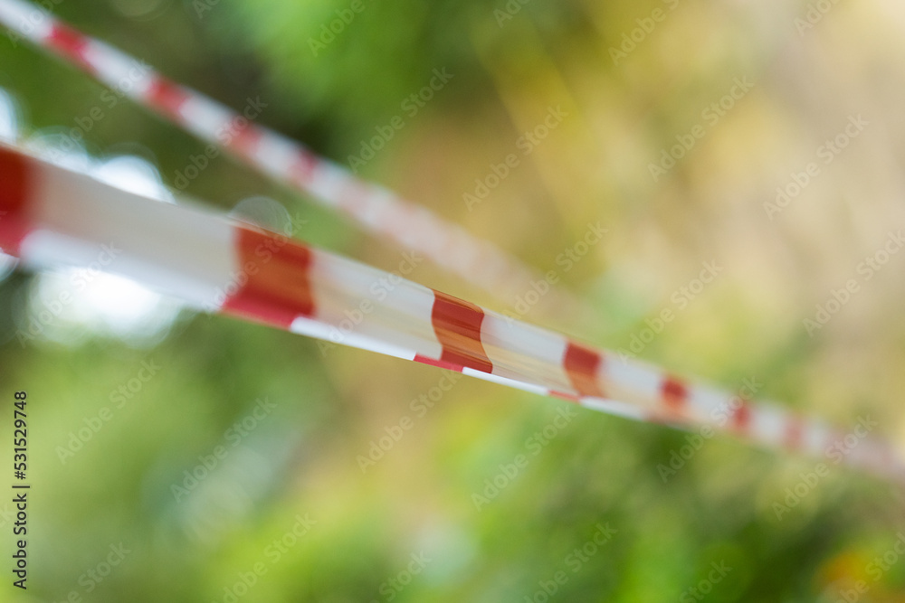White-red protective tape. Barrier tape on a green background. White and red strip barrier tape. White-red protective tape. Barrier tape on a green background. White and red strip barrier tape.