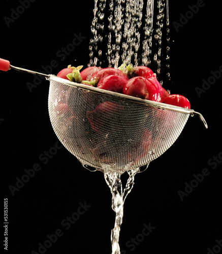 washing radish in a colander on black background.