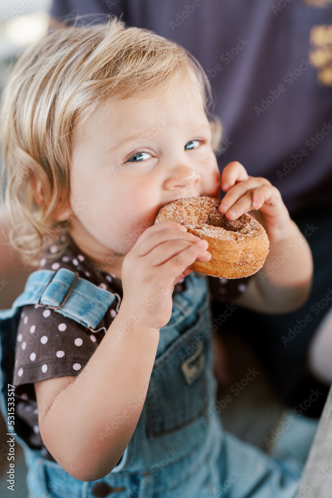 A cute toddler girl holding and eating a cinnamon sugar donut A cute toddler girl holding and eating a cinnamon sugar donut
