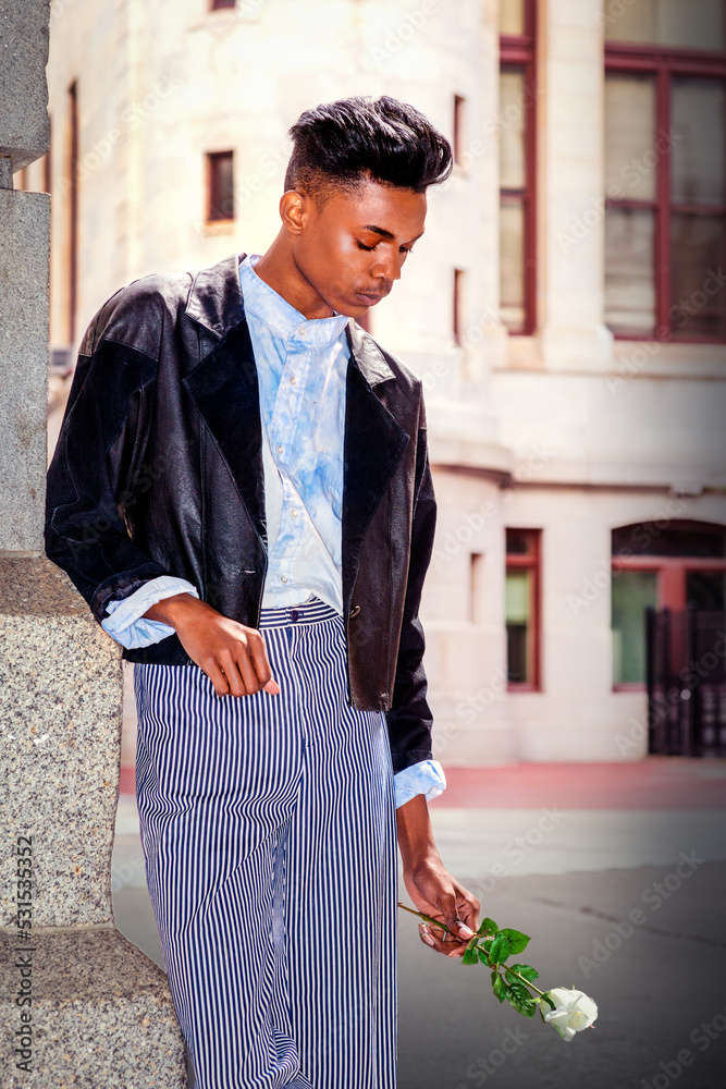 Lonely boy. A 18 years old student, wearing a fashionable black jacket, striped pants, a blue-dyed white shirt, is standing by the gate on campus, holding a white rose, lower his head, sad, thinking.