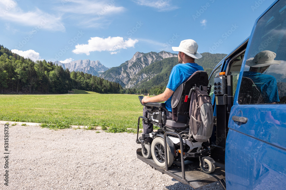 Man with disability a frequent traveller, getting off a van using the wheelchair lift after arriving in a mountain rest area