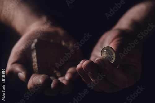 Fototapeta Hungry man holding euro money and bread on a black background, hands with food close-up