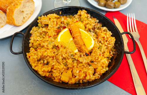 Tasty Valencian paella marinera with shrimps and scallop served with lemon on iron frypan