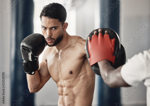 Fitness, training and a man boxing in gym with personal trainer and sparring pads. Health, motivation and exercise, boxer throwing a punch. Fight, muscle and workout with sports gloves in mma studio.