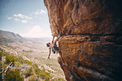 Rock climbing, rope and fearless mountain climber on a cliff, big rocks and risky challenge alone in summer. Mountaineering, bouldering and strong man training his body for balance outdoors in nature