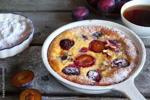 Damson blue plum clafoutis (flan) and cup of tea, icing sugar and almonds dressing