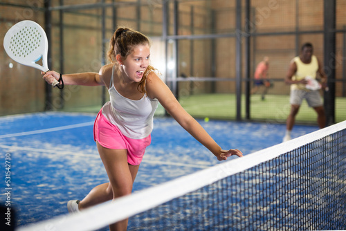 Expressive resolved young fit girl playing paddle ball friendly match on small closed court. Concept of competition emotions.