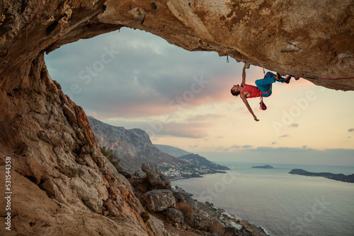 Male rock climber climbing along a roof in cave at sunset