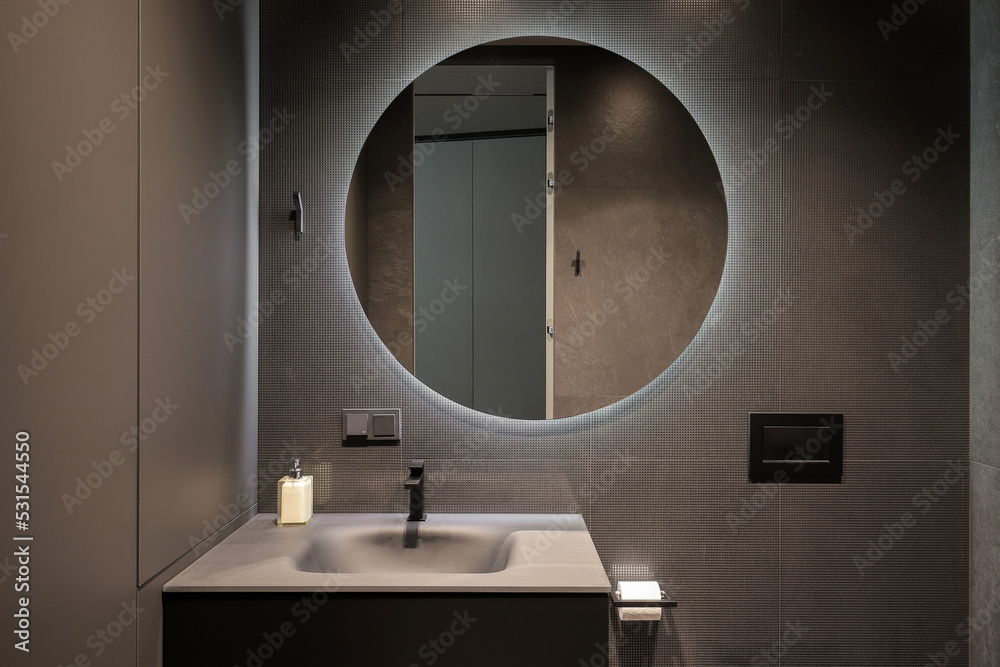Illuminated round mirror in a dark bathroom interior - obrazy, fototapety, plakaty 