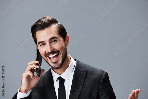 Portrait of business man with phone conversation and smile with teeth on gray background in business suit. Business portrait of a stylish man copy space