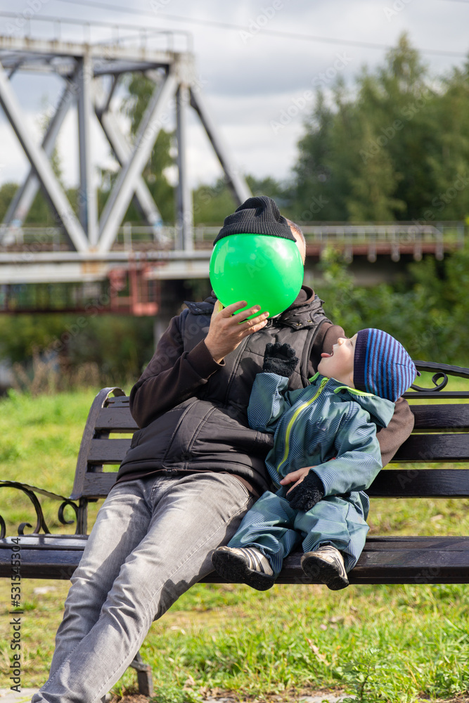 Fototapeta premium Father and son play with a ball on a bench in autumn. Entertainment with parents. Happy family on the street.