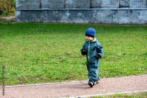 A two-year-old little toddler boy runs along a sand path alone into the unknown.