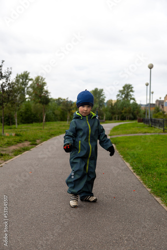 
A two-year-old boy in autumn on the road with a rowan branch in his hands smiles on the street
