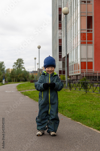 
A two-year-old boy in autumn on the road with a rowan branch in his hands smiles on the street