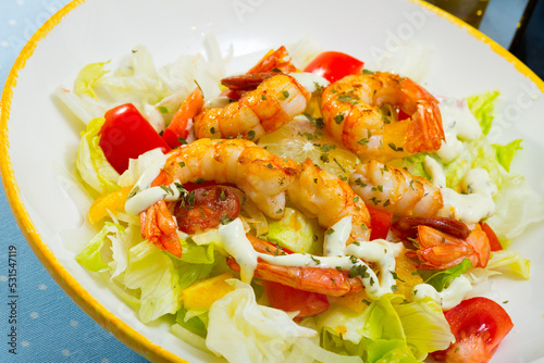 Appetizing salad with grilled shrimps, chorizo sausage, vegetables and lemon served on white plate