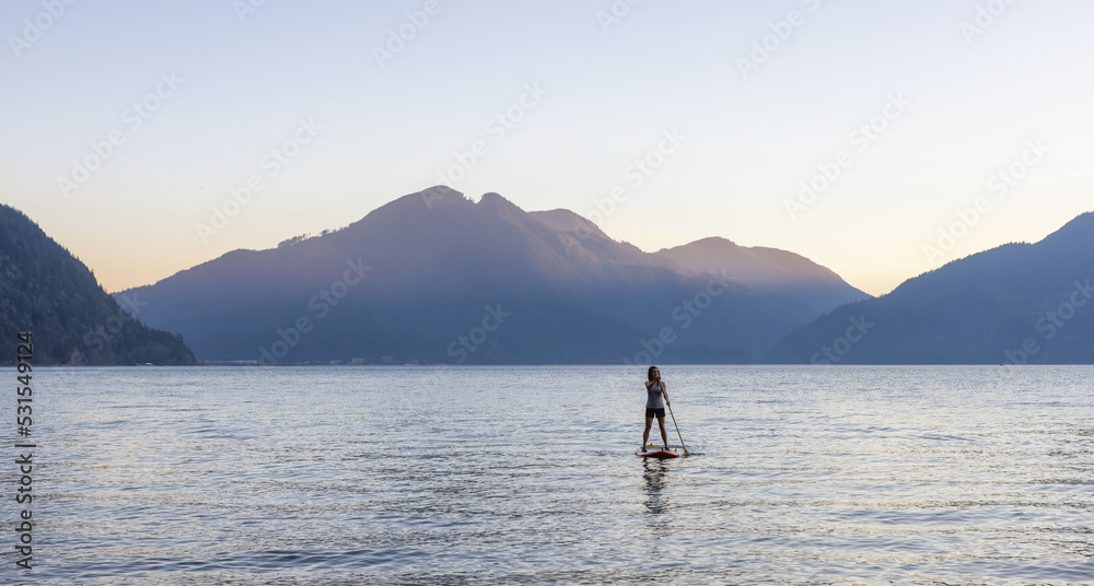 Adventurous Woman Paddling on a Paddle Board in a peaceful lake.