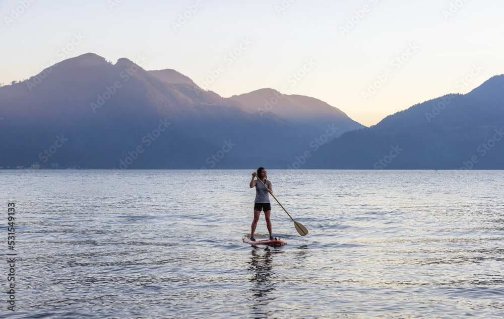 Naklejka premium Adventurous Woman Paddling on a Paddle Board in a peaceful lake.