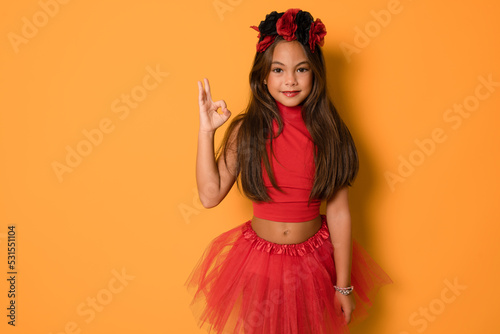 Beautiful little kid girl in halloween costume showing okay sign isolated over orange background. Halloween concept.