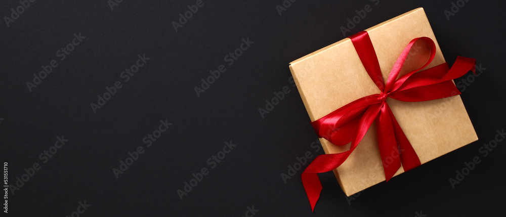 Black Friday sale banner design. Craft paper gift box wrapped red ribbon bow on black background. Black Friday sale banner design. Craft paper gift box wrapped red ribbon bow on black background.