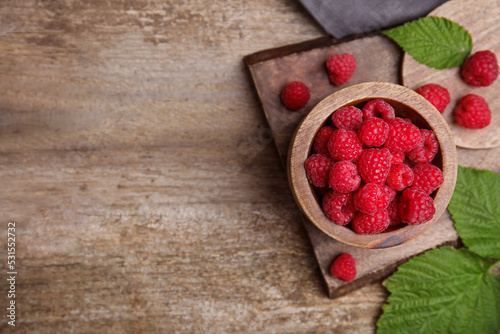 Bowl with fresh ripe raspberries and green leaves on wooden table, flat lay. Space for text