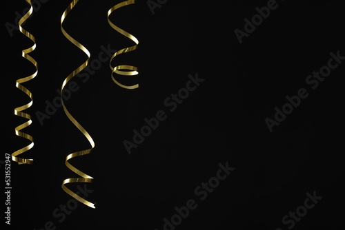 Shiny golden serpentine streamers on black background. Space for text