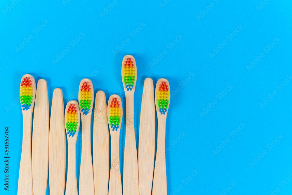 Lot of ecological new bamboo toothbrushes on blue background top view. Composition of bright wooden brushes laid out in chaotic row. Set of bright wooden toothbrushes for children. Eco oral hygiene. Lot of ecological new bamboo toothbrushes on blue background top view. Composition of bright wooden brushes laid out in chaotic row. Set of bright wooden toothbrushes for children. Eco oral hygiene.