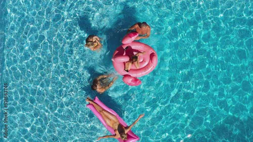 Overhead drone shot of multi-generation family with baby boy on summer holiday relaxing on inflatables and splashing in swimming pool - shot in slow motion Overhead drone shot of multi-generation family with baby boy on summer holiday relaxing on inflatables and splashing in swimming pool - shot in slow motion