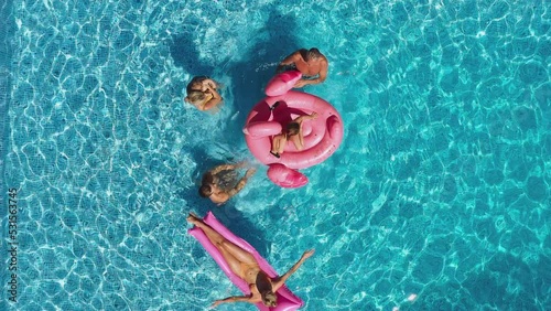 Overhead drone shot of multi-generation family with baby boy on summer holiday relaxing on inflatables and splashing in swimming pool - shot in slow motion