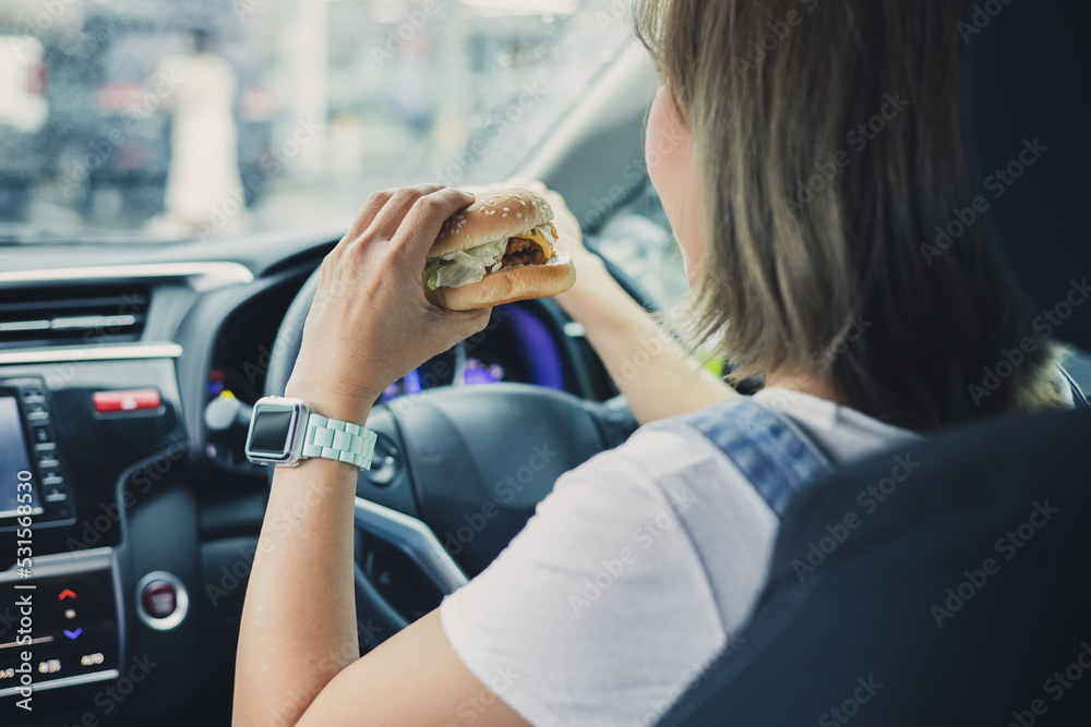 woman eating burger while driving car in the city. woman eating burger while driving car in the city.