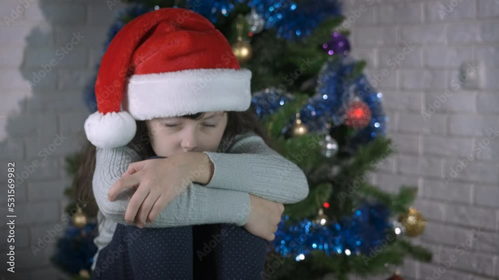 Upset and offended Santa child. An upset little girl hide her face and cry on the floor by the New Year colorful tree. Upset and offended Santa child. An upset little girl hide her face and cry on the floor by the New Year colorful tree.